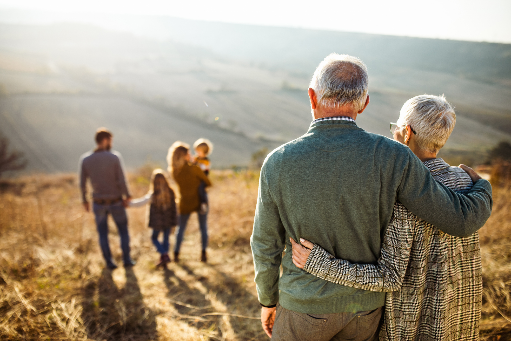 Senior couple embracing outdoors, looking at their family